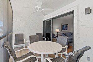 Un balcón con mobiliario de mimbre, ventilador de techo y vista hacia una habitación con sofá y lámpara.