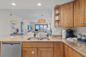 A modern kitchen with wooden cabinets, a granite countertop, stainless steel appliances, and a view to the living area.