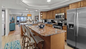 A modern kitchen with wooden cabinets, stainless steel appliances, a large island with bar stools, and a ceiling fan. - Modern Gulf-Front Condo in Sanibel – Newly Renovated & Ready for Your Escape (Sanibel)