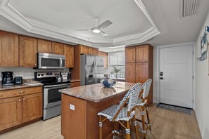 Una cocina con armarios de madera, electrodomésticos de acero inoxidable, una isla central con taburetes y un ventilador de techo.
