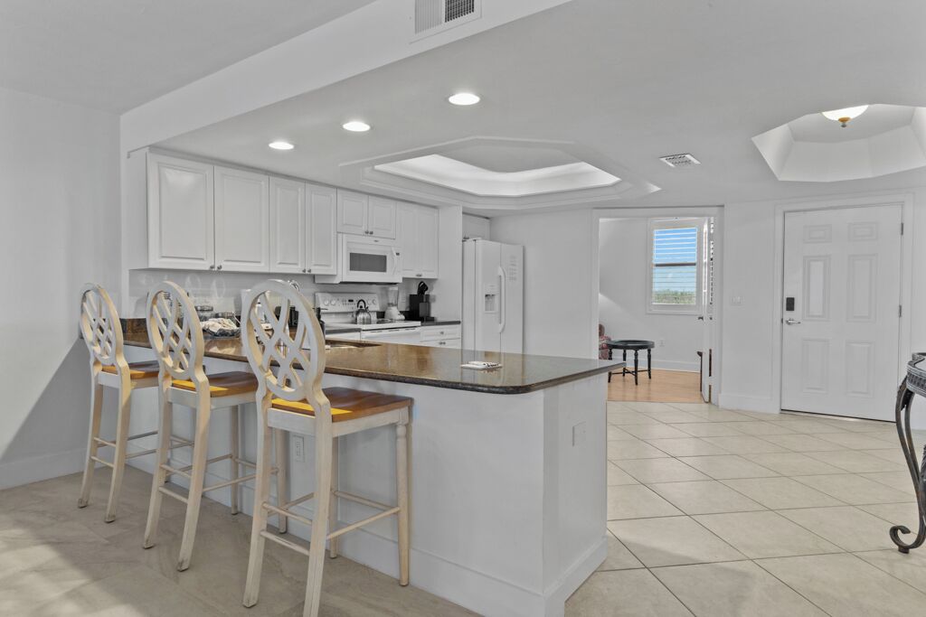 A modern kitchen with white cabinets, a central island with bar stools, and recessed ceiling lights.