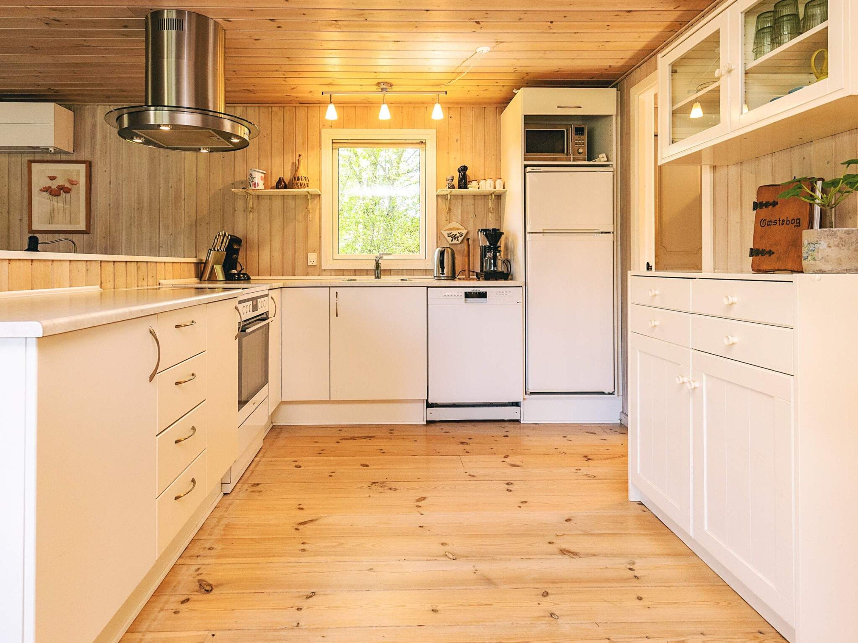 A kitchen with wooden cabinets, a stainless steel range hood, a microwave, and a refrigerator.
