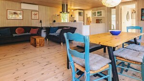 A cozy cabin interior with a wooden dining table, blue chairs, a sofa, and a kitchen area. - 6 Person Holiday Home in Hals (Hals)