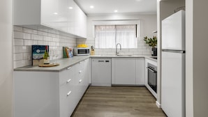 A modern kitchen with white cabinetry, a built-in microwave, and a dishwasher. - Banksia Rosebud  Pet Friendly (Rosebud)
