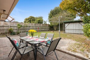 An outdoor patio with a table set for dining, surrounded by chairs.