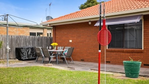 A backyard with a tennis net, a table with chairs, and a potted plant. - Banksia Rosebud  Pet Friendly (Rosebud)
