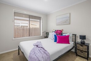 Ein Schlafzimmer mit Bett, Fenster mit Jalousien, Nachttisch mit Lampe und einem Wandbild.