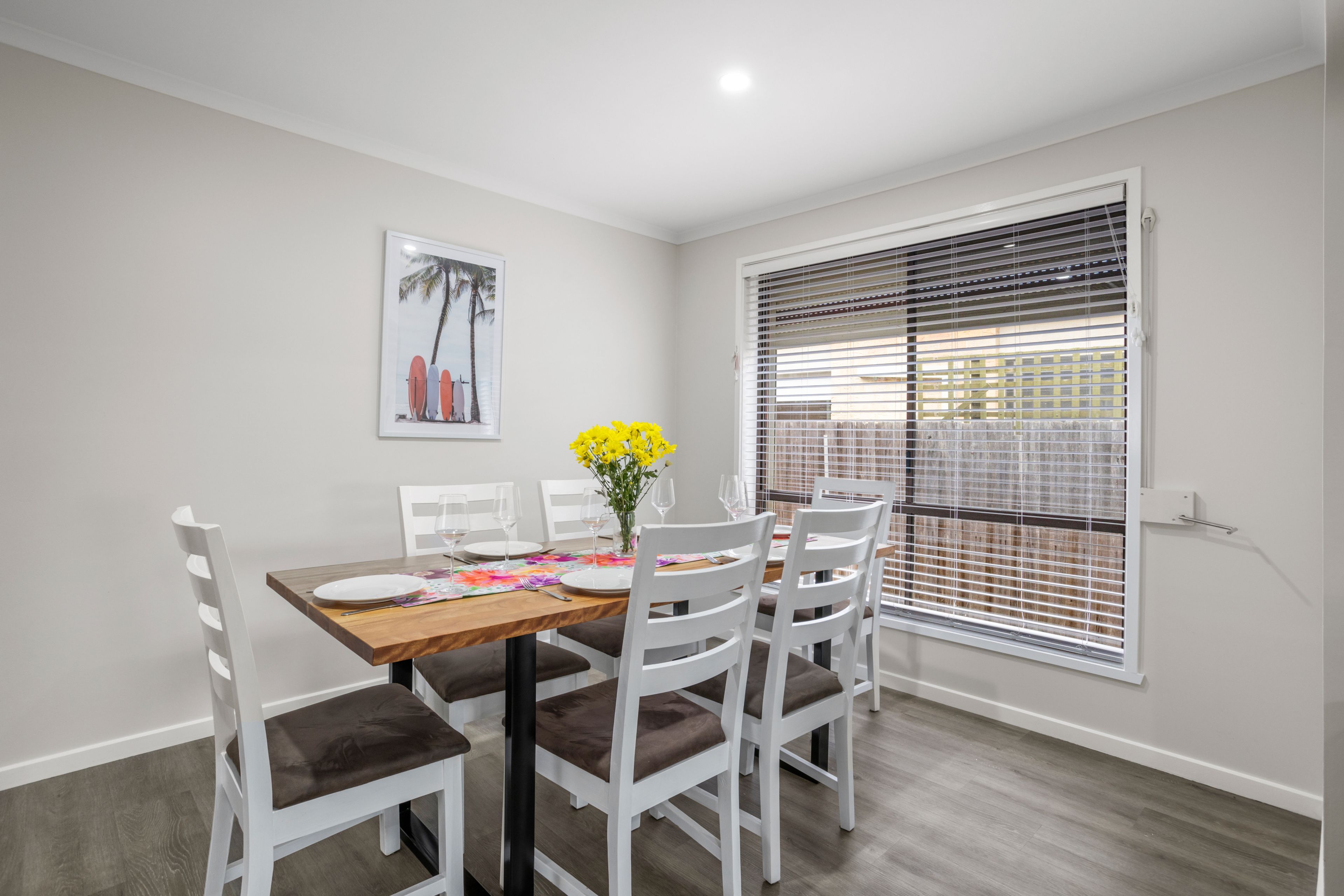 A dining area with a wooden table, white chairs, and a framed picture on the wall.