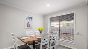 A dining area with a wooden table, white chairs, and a framed picture on the wall. - Banksia Rosebud  Pet Friendly (Rosebud)