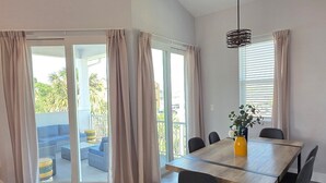 Un espace repas moderne avec une table en bois et des chaises noires, de grandes portes-fenêtres coulissantes donnant sur un espace extérieur aménagé, et un luminaire suspendu.