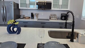 Une cuisine moderne dotée d’un réfrigérateur en acier inoxydable, de meubles blancs, d’un robinet noir et d’un luminaire original.