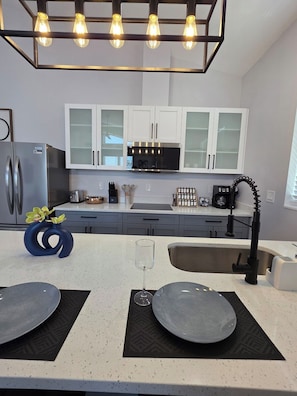 Una cocina moderna con refrigerador de acero inoxidable, armarios blancos, grifo negro y una lámpara original.