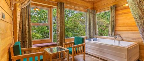 A wooden cabin interior with a bathtub, wooden furniture, and large windows.