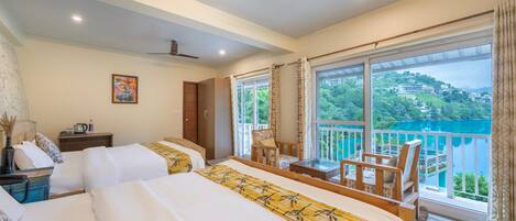A hotel room with two beds, a balcony with a view of a lake, and a ceiling fan.