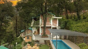 Une maison avec une piscine, entourée d’une végétation luxuriante et agrémentée d’un petit jardin avec du mobilier d’extérieur.