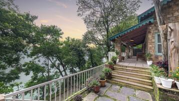 A stone staircase leading to a wooden building with a green roof, surrounded by lush greenery and a view of a body of water.
