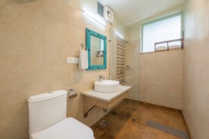 A bathroom with a toilet, sink, mirror, shower, and a window.