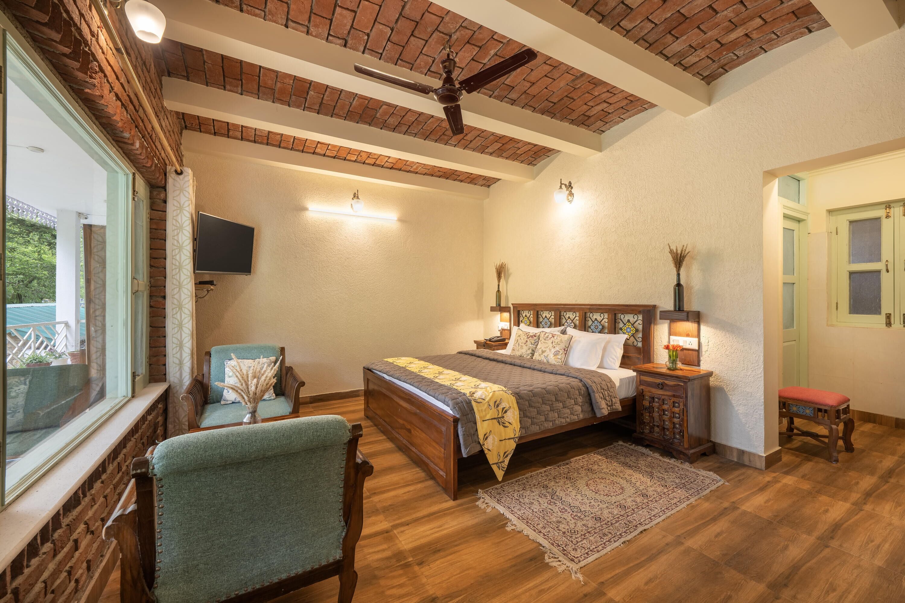 A bedroom with a brick ceiling, a bed with a headboard, a TV mounted on the wall, and a window with a view of greenery.