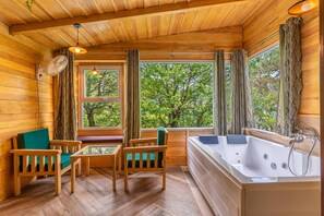 A wooden cabin interior with a wooden floor, a sofa, a table, a bathtub, and large windows with curtains. - Echor Malusara Lakeview Retreat Bhimtal (Bhimtal)