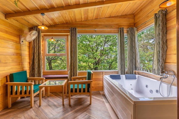 A wooden cabin interior with a wooden floor, a sofa, a table, a bathtub, and large windows with curtains. - Echor Malusara Lakeview Retreat Bhimtal (Bhimtal)