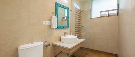 A bathroom with a toilet, sink, mirror, shower, and a window.