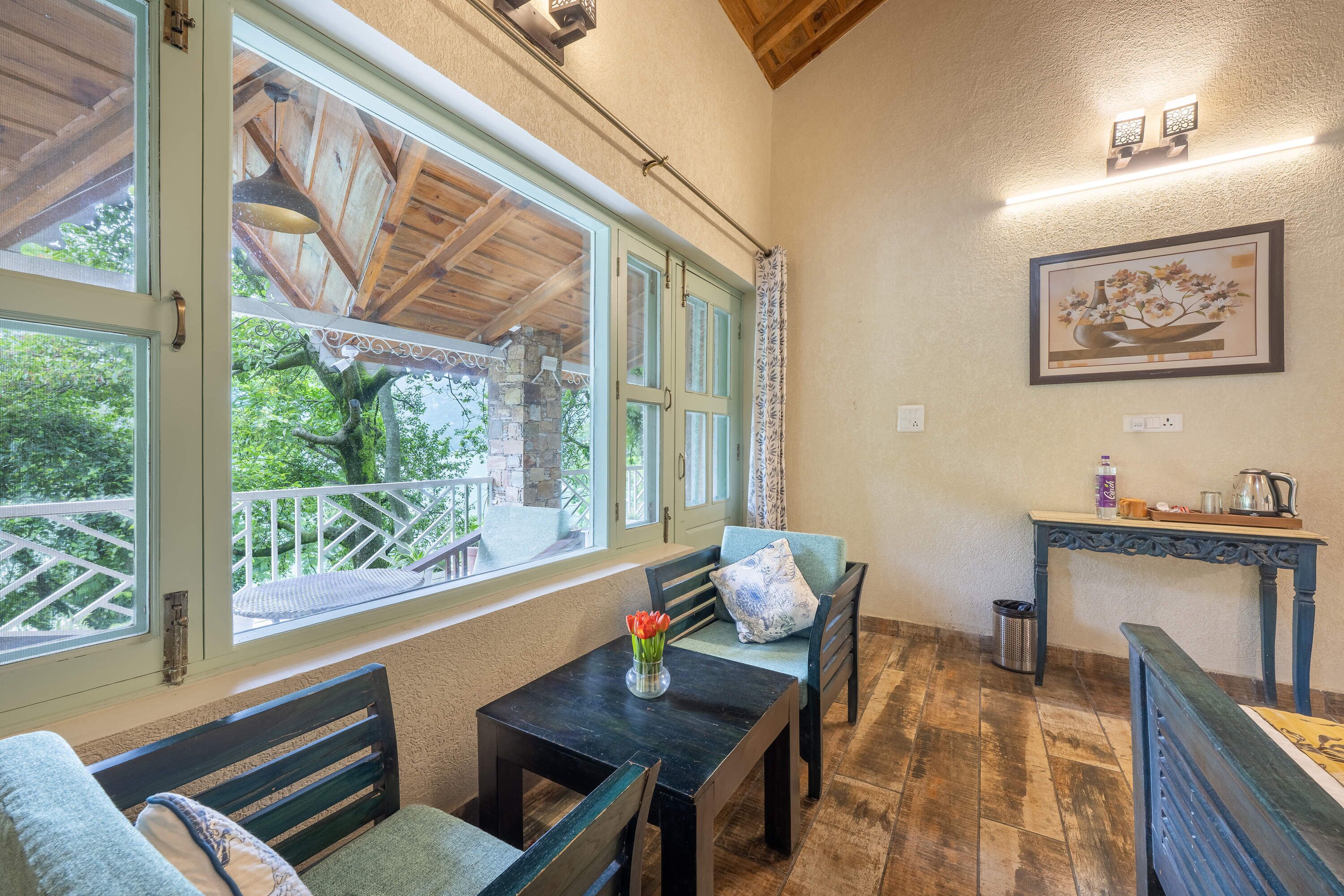 Una habitación acogedora con techo de madera, una mesa con sillas, un jarrón de flores y un cuadro en la pared.