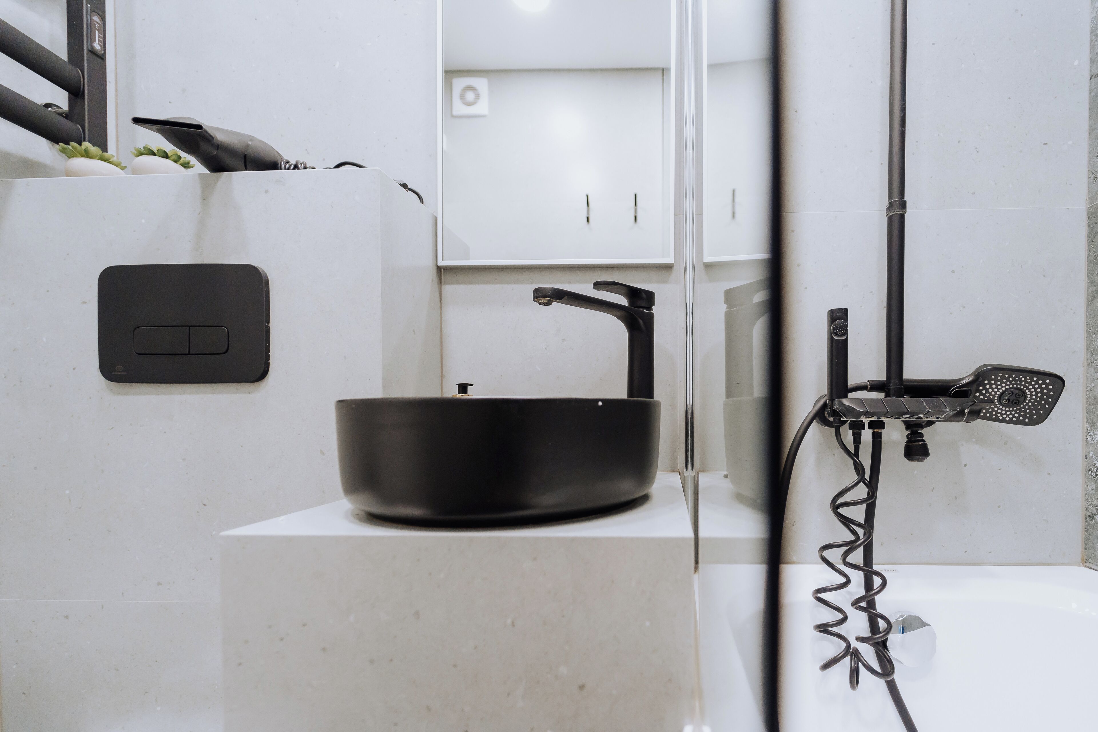 Ein modernes Badezimmer mit einem schwarzen Waschbecken auf einer weißen Arbeitsplatte, einer Handbrause und einer wandmontierten Lampe.