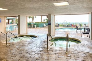 Espaço de piscina interna com duas banheiras de hidromassagem, um bar e área externa com mesas e cadeiras.