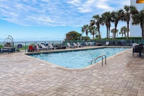 A pool area with lounge chairs, a pool, and a view of the ocean. - Oceanfront studio with private balcony, pool, beach access, & snowbird friendly (Myrtle Beach)