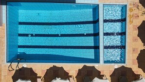 A swimming pool with multiple lanes, tiled walls, and sun umbrellas. - AVENA Suites (Kato Gouves)