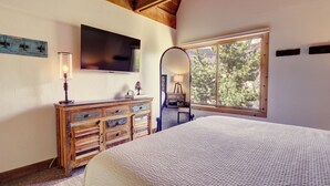 A bedroom with a large bed, wooden dresser, TV, and a window with a view of trees.