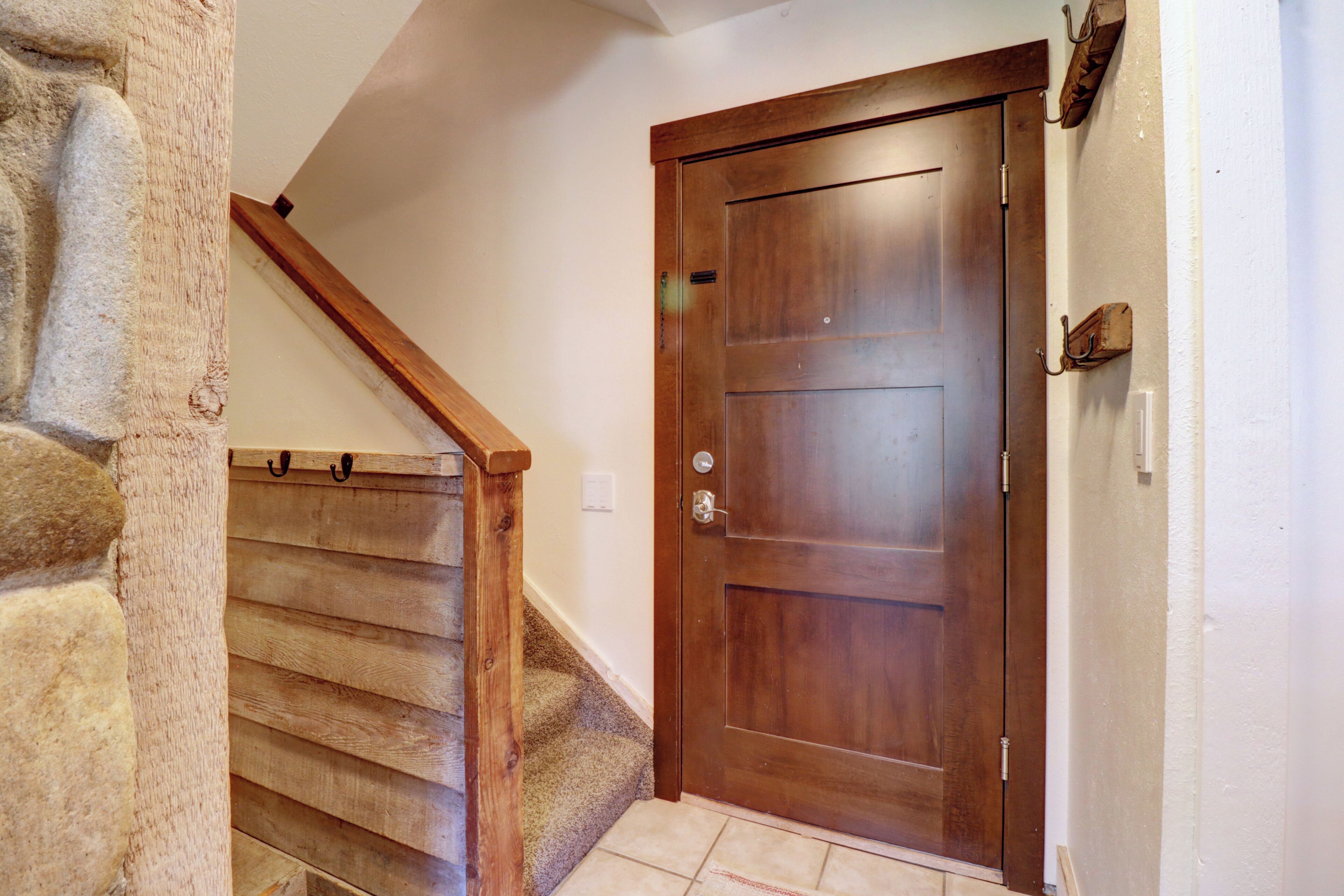 Eine Holztür mit Metallbeschlag, eine Steinwand und eine Holztreppe mit Handlauf.