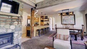 A spacious living area with a stone fireplace, a wooden dining table with chairs, and a kitchen in the background.