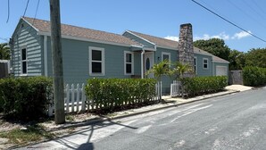 A single-story house with a gabled roof, a stone chimney, and a white picket fence.