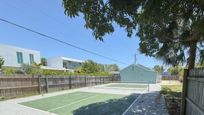 A tennis court with a wooden fence, a shed, and a house in the background.