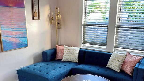 A modern living room with a blue sectional sofa, a round coffee table, and a large painting on the wall.