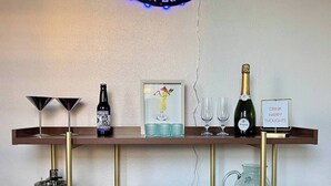 A bar area with a neon sign, a bottle of liquor, glasses, and a sign that says "DRINK HAPPY THOUGHTS".