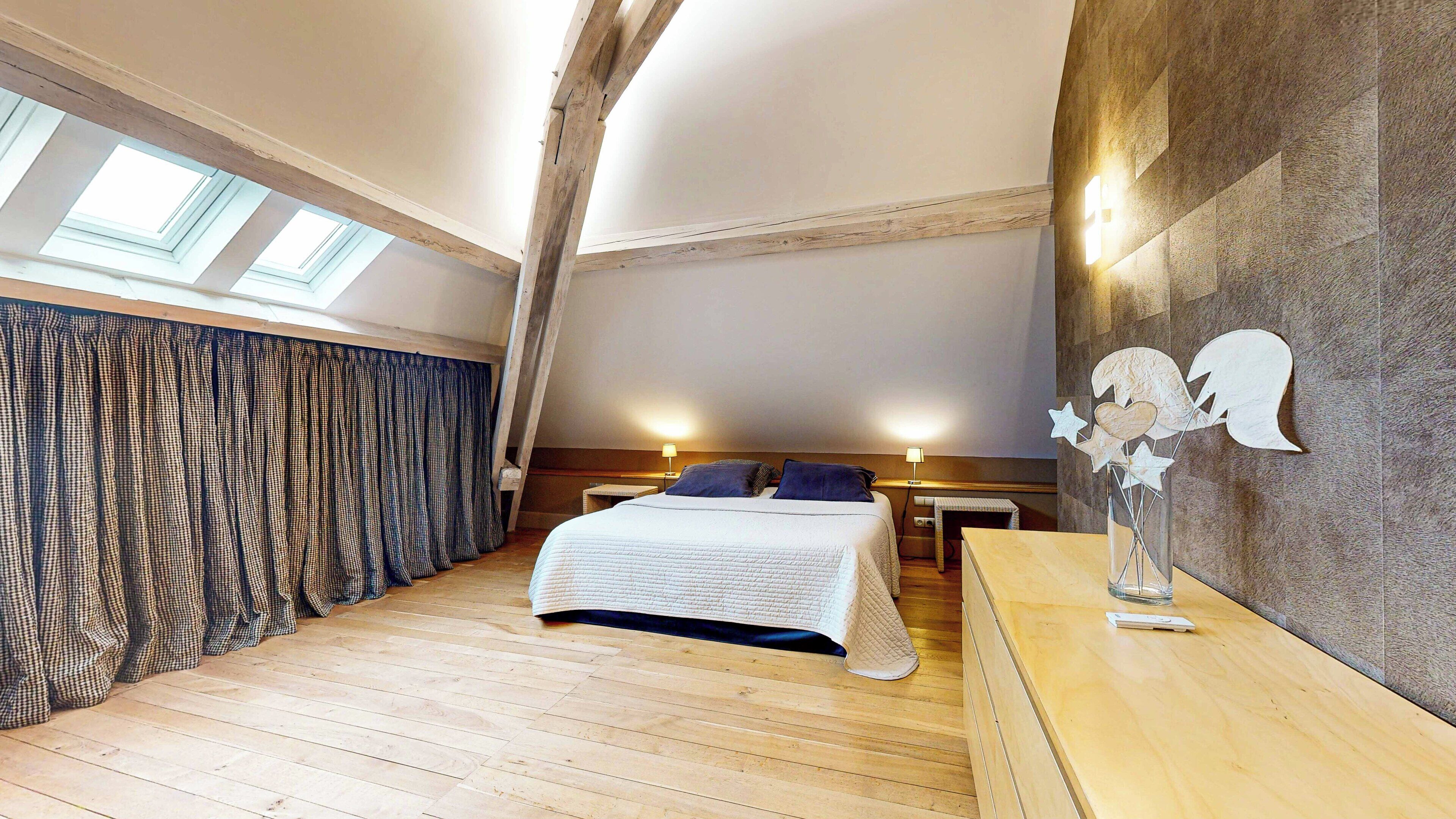 A bedroom with a bed, a nightstand, a desk, a lamp, and a wall-mounted light fixture.