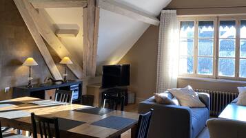 A cozy loft-style room with a dining area, a sofa, and a television.