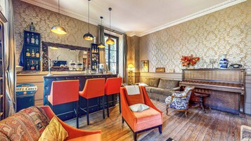 Zona de bar con mostrador, taburetes y un piano. Hay dos sofás y un sillón estampado.