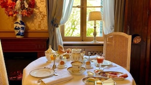 A dining table set for breakfast with tea, eggs, and pastries, a vase of flowers, and a view of trees through a window. - Demeure Saint Louis (Carcassonne)