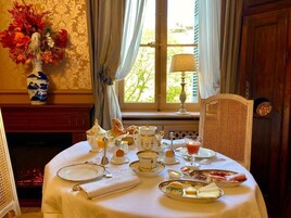 Una mesa de desayuno dispuesta con té, huevos y pasteles, un jarrón de flores y vistas a árboles a través de una ventana.