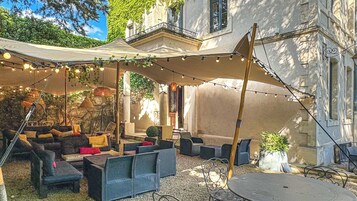 Un patio exterior con mobiliario de mimbre, luces colgantes y una zona cubierta.