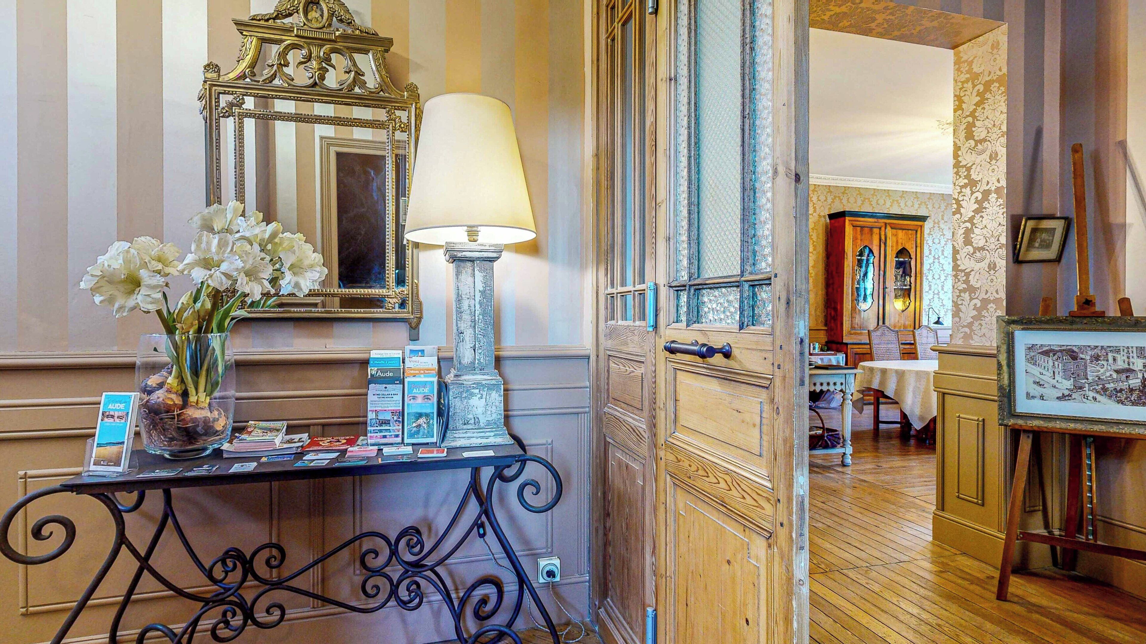 A reception area with a mirror, a lamp, a vase with flowers, and a table with brochures.