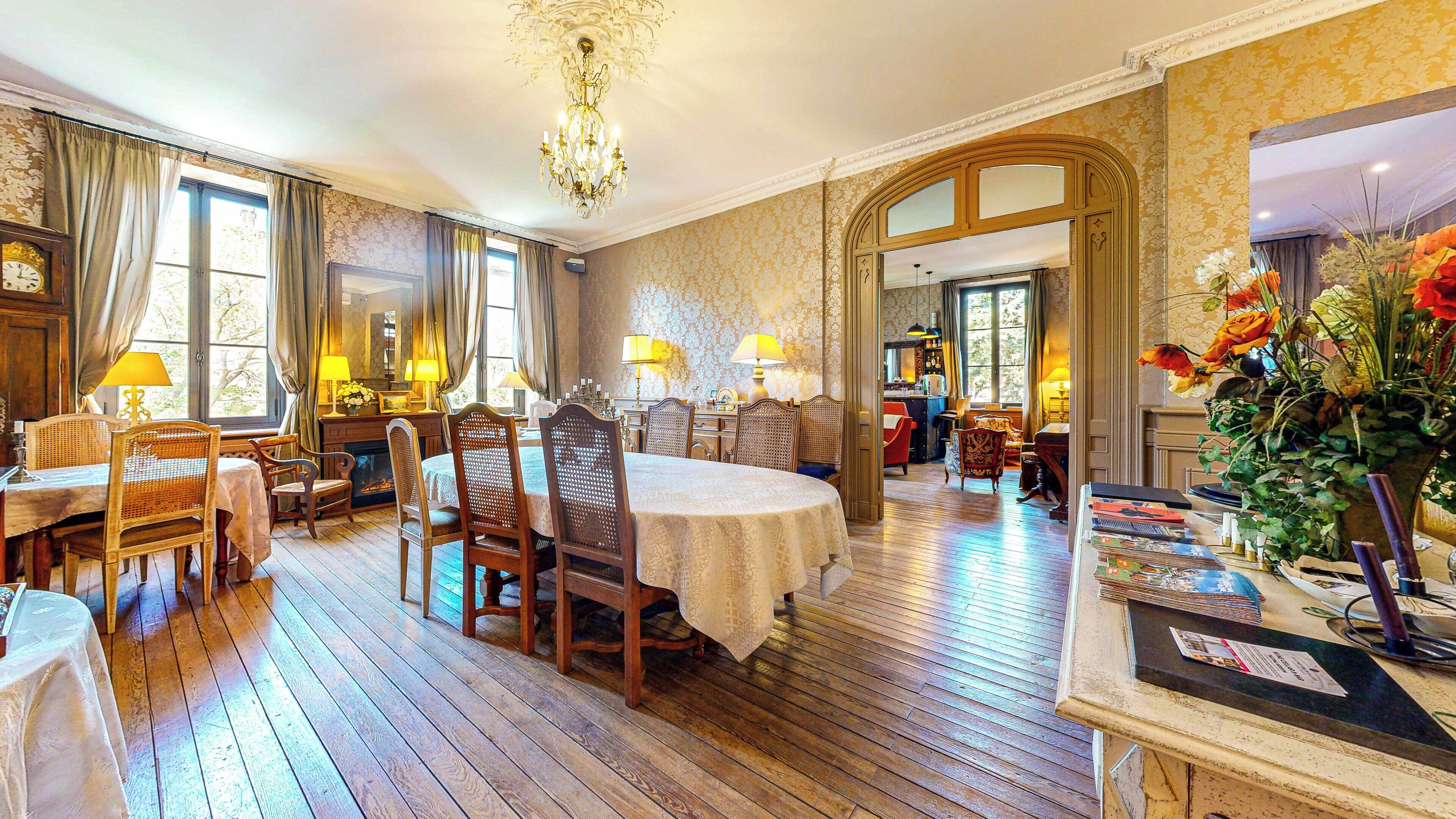 A spacious dining area with a round table, wooden chairs, and a chandelier.
