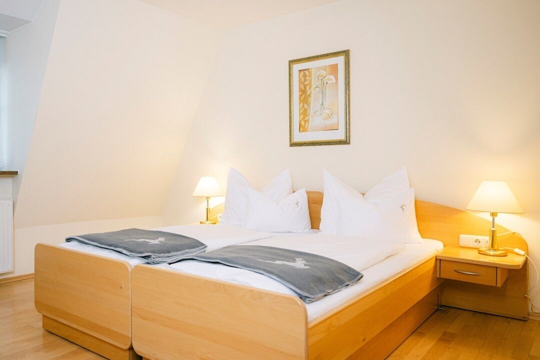 Un lit double avec un cadre en bois, deux tables de chevet avec des lampes, un tableau encadré au mur et une fenêtre sur le côté gauche.