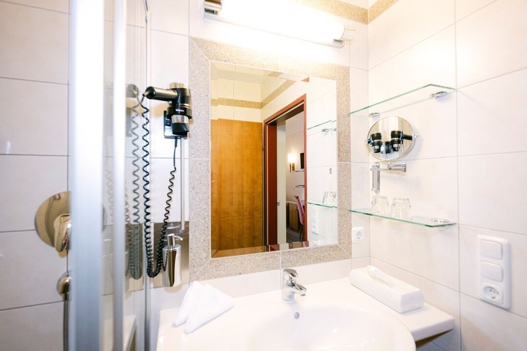 Ein modernes Badezimmer mit Duschkabine aus Glas, großem Spiegel und weißem Waschbecken mit Handtuch und Seifenspender.