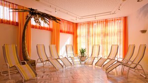 A room with a tiled floor, multiple sun loungers, and a large plant. - Hotel Jägerwirt (Lengau)