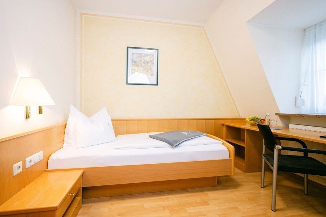Une chambre d’hôtel de taille réduite, comprenant un lit, un bureau, une chaise et une petite table.