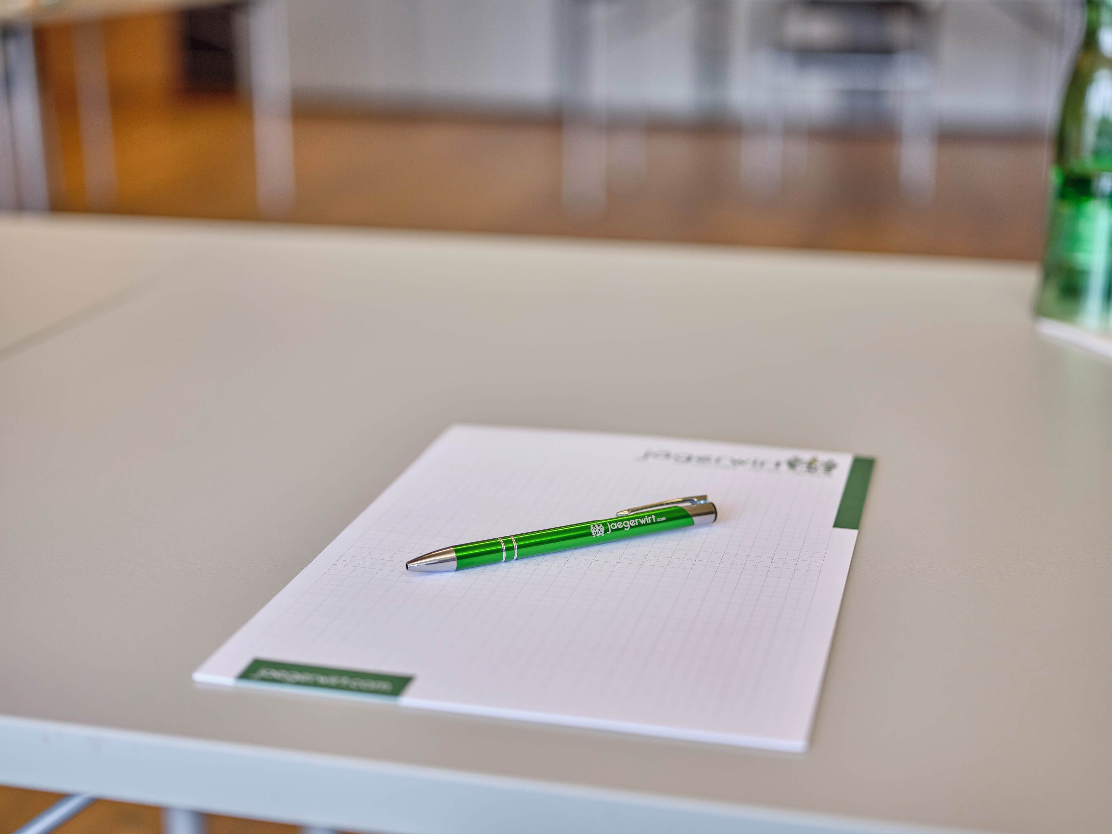 Un stylo vert posé sur une feuille de papier quadrillée, lui-même placé sur une table blanche.